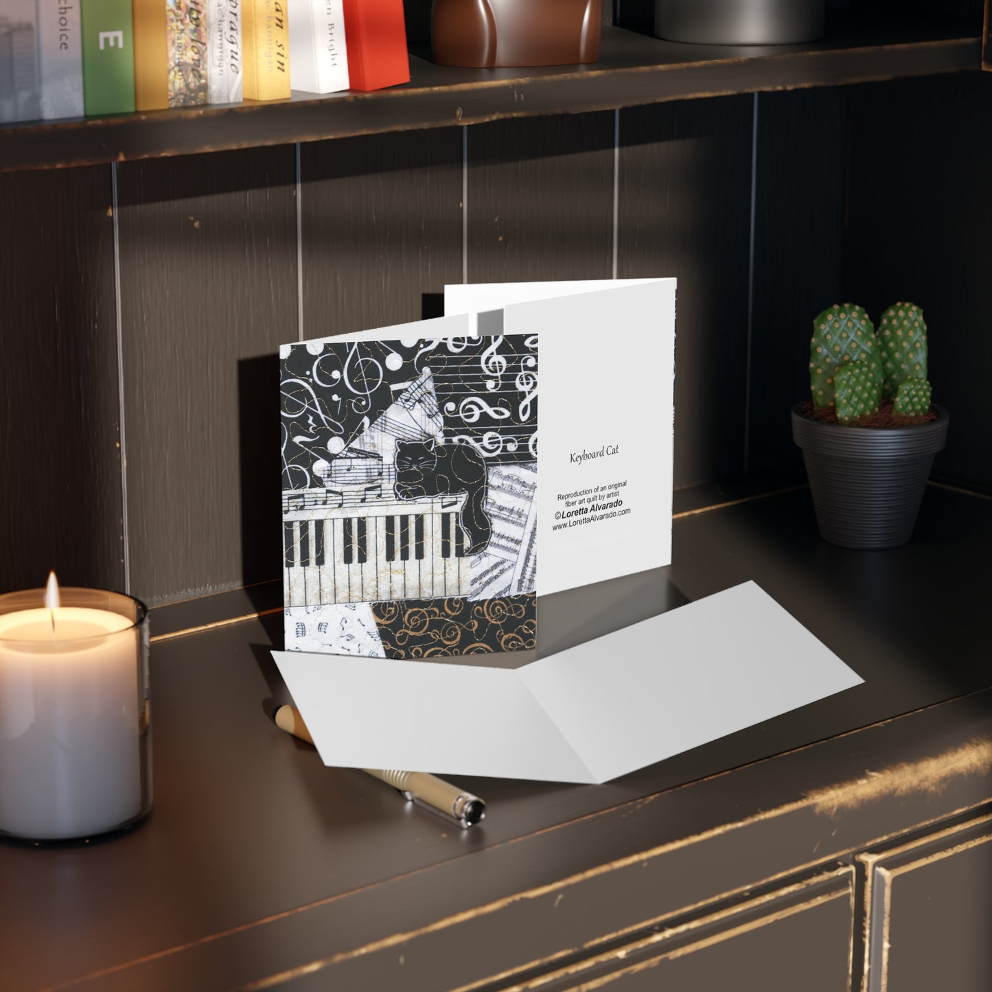 Greeting card with a black cat on a  piano keyboard design on a dark surface next to a candle and plant