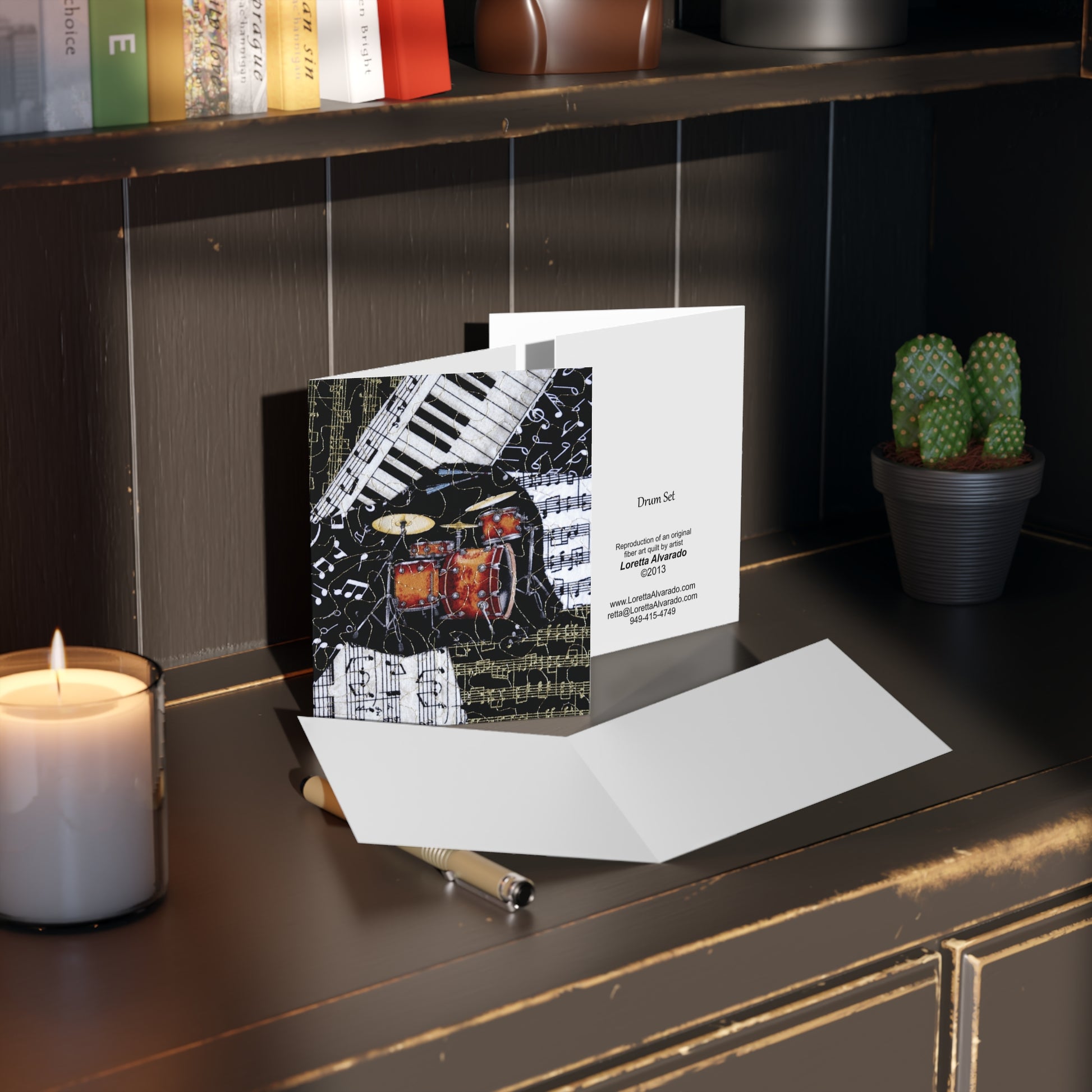 Greeting card with a drum kit design on a desk with a candle and plant.