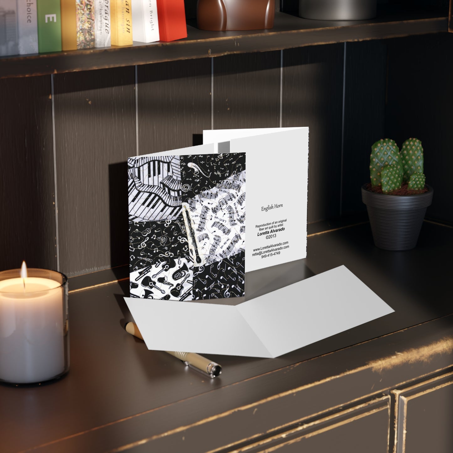 Greeting card with black and white music-themed English horn design on a desk next to a candle and potted plant.