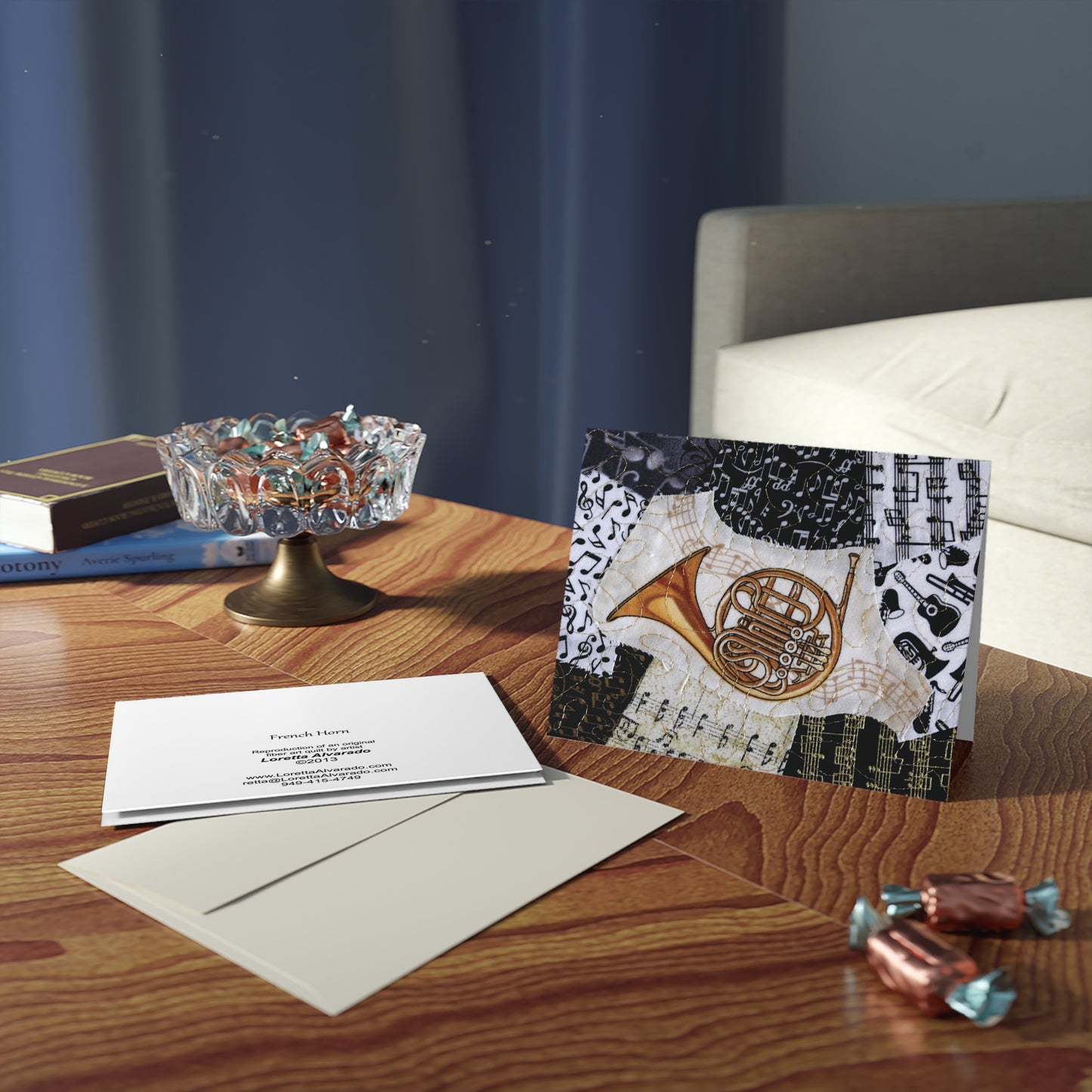 Greeting card with musical design featuring a French horn on a wooden surface with books and candies.